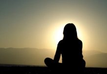 Explicación científica de por qué la meditación te ayuda a cometer menos errores Mujer meditando al atardecer frente al mar con el sol poniéndose tras montañas
