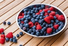 Alimentos ricos en flavonoides reducen el riesgo de Alzheimer Cuenco con arándanos y frambuesas sobre mesa de madera
