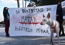 “Ni serio ni riguroso: un documento para lavar la imagen de la caza y apoyar el modelo intensivo de explotación cinegética” Mujeres con un perro blanco portan un cartel contra la caza que dice: "Si disfrutas de matar, háztelo mirar"