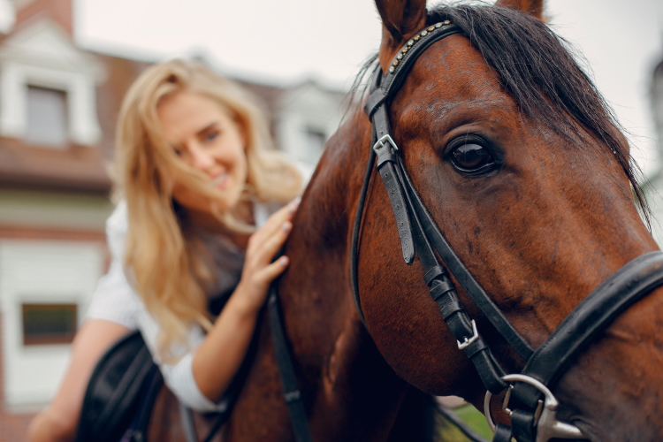 Mujer con vestido blanco cabalga caballo marrón. Vemos cabeza de caballo en primer plano